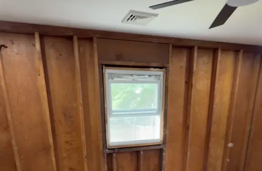 Room stripped down to wood paneling and studs during demolition, with insulation debris on the floor