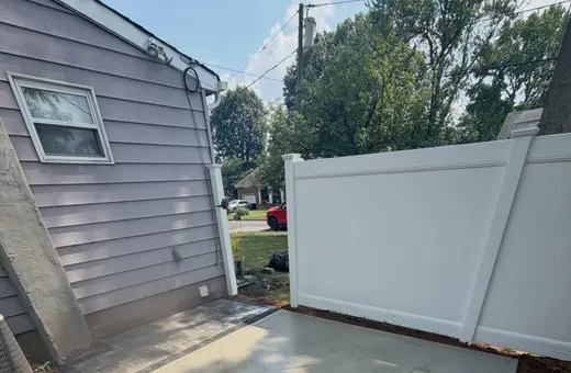 New composite deck stairs with white vinyl railings leading up to a back door on a blue shingle-sided home