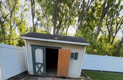 Older wood storage shed with a hinged door standing open in a fenced backyard