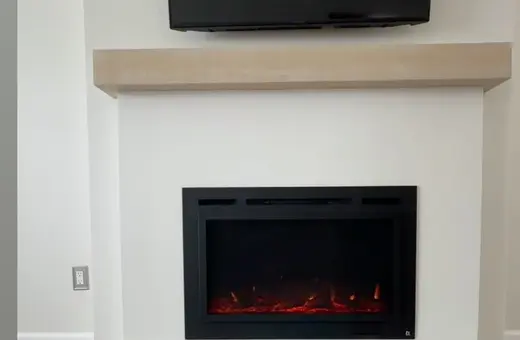 Modern living room fireplace with black electric insert, light wood mantel, and gray luxury vinyl plank flooring