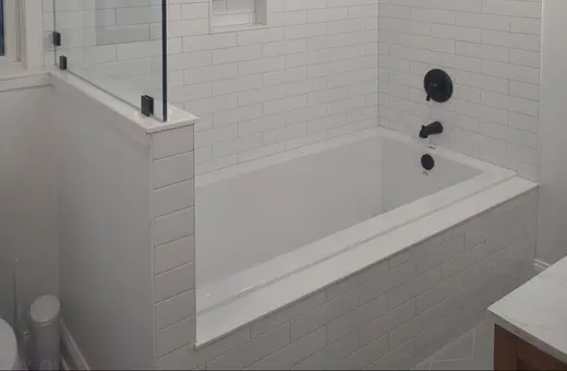 Finished bathroom with white subway tile tub-shower surround, frameless glass panel, and matte black fixtures