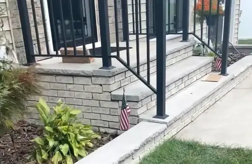 Close-up of new concrete steps with brick veneer risers and black metal railings leading to a front porch