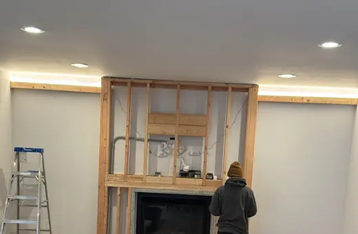 Contractor framing a new wall around a fireplace insert, with fresh hardwood flooring installed in the room