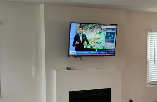 Living room fireplace renovation nearing completion, with a mounted TV, white surround, and new plank flooring