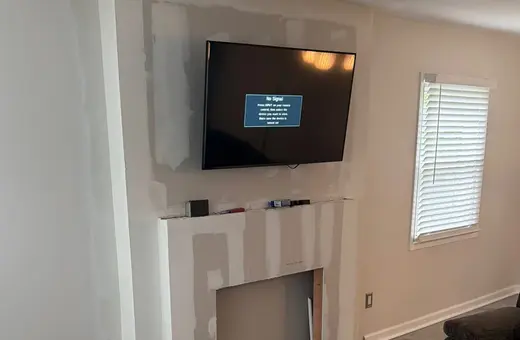 Fireplace surround finished in drywall and ready for paint, below a mounted TV and new plank flooring